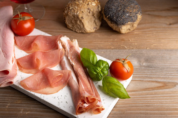 Antipasto table with smoked and cooked ham and bread on a plate with a glass of red wine on the side.