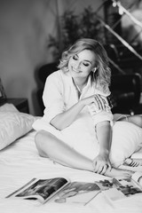 Beautiful blonde woman in the morning in bed in a white shirt in headphones listens to music eats chocolate and smiles. Black and white photo..