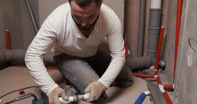 Plumber is working in spacious bathroom, soldering pipes, laying new sewers, welding plastic pipes, cooling joints, repairs in apartment, hot and cold water pipes, bearded man, serious professional