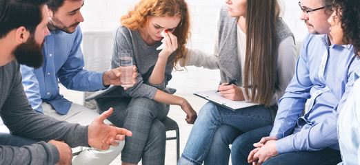 Rehab community members supporting crying emotional woman at group therapy session