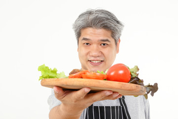 Fat old man holds a wooden tray with fresh vegetables for water to cook. The concept of healthy eating for the elderly. White background