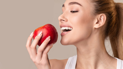 Young Lady Biting Red Apple On Beige Studio Background, Panorama