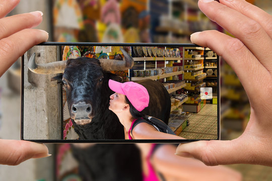 Photographing on cell phone women kissing bull on vacation in Spain.