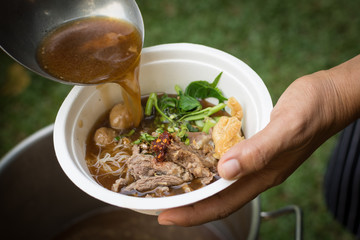 pouring soup with a ladle in a bowl with Thai beef noodle soup (ก๋วยเตี๋ยวเนื้อน้ําใส)