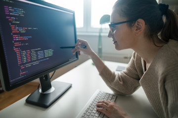 Young woman programming at her home office. Female programmer ponting at computer codes