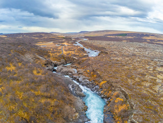 Hraunfossar series of waterfalls barnafoss aerial image of turquoise water streaming down gaps in lava field during autumn