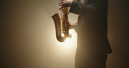 A saxophonist wearing a suit performing a solo on stage, spotted and silhouetted by light - arts, jazz music concept 4k footage