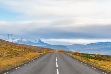 Roadtrip in Iceland empty paved road leading over mountains with snow covered tips next to power line in autumn