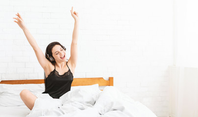 Fototapeta na wymiar Energetic woman dancing in bed, listening to music