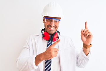 Young chemist man wearing security helmet and headphones over isolated background smiling and looking at the camera pointing with two hands and fingers to the side.