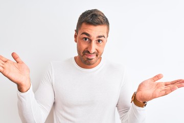 Young handsome man wearing white shirt over isolated background clueless and confused expression with arms and hands raised. Doubt concept.