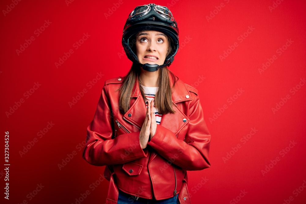 Wall mural Young beautiful brunette motocyclist woman wearing motorcycle helmet and red jacket begging and praying with hands together with hope expression on face very emotional and worried. Begging. - Wall murals