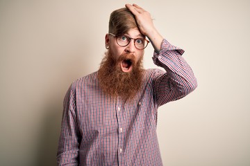 Handsome Irish redhead business man with beard wearing glasses over isolated background surprised...