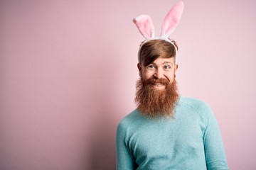 Hipster Irish man with beard wearing easter rabbit ears over isolated pink background with a happy and cool smile on face. Lucky person.
