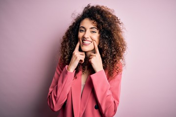 Young beautiful businesswoman with curly hair and piercing wearing elegant jacket Smiling with open mouth, fingers pointing and forcing cheerful smile