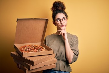 Young beautiful woman with curly hair and piercing holding delivery boxes with Italian pizza...