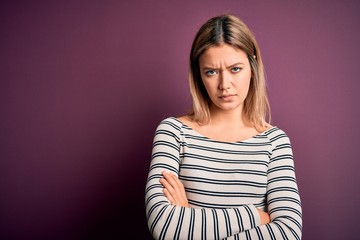 Young beautiful blonde woman wearing casual striped shirt over purple isolated background skeptic and nervous, disapproving expression on face with crossed arms. Negative person.