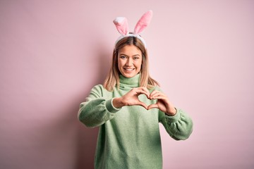 Young beautiful woman wearing easter rabbit ears standing over isolated pink background smiling in...