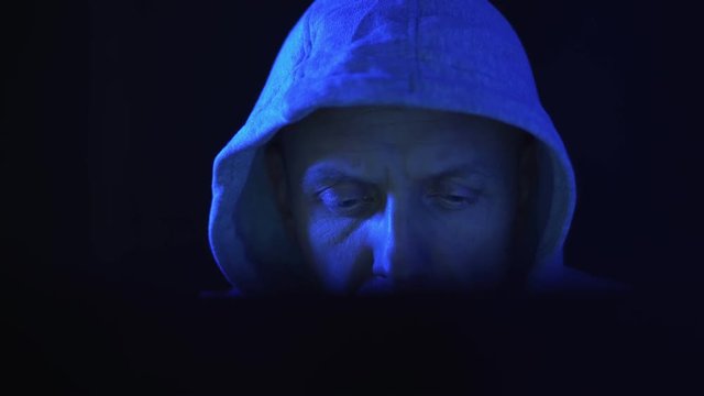A hacker programmer, at night at a laptop computer, creates virus hacking programs. In the dark blue light.