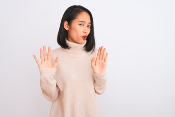 Young chinese woman wearing turtleneck sweater standing over isolated white background Moving away hands palms showing refusal and denial with afraid and disgusting expression. Stop and forbidden.