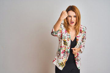 Young caucasian business woman wearing spring floral jacket suit over isolated background angry and mad raising fist frustrated and furious while shouting with anger. Rage and aggressive concept.