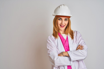 Redhead caucasian woman engineer wearing safety helmet over isolated background happy face smiling with crossed arms looking at the camera. Positive person.
