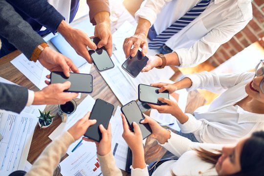 Group of business workers standing with hands together using smartphone doing symbol at the office