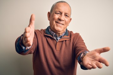 Naklejka premium Senior handsome man wearing elegant sweater standing over isolated white background looking at the camera smiling with open arms for hug. Cheerful expression embracing happiness.