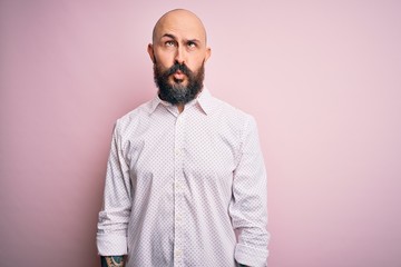 Handsome bald man with beard wearing elegant shirt over isolated pink background making fish face with lips, crazy and comical gesture. Funny expression.