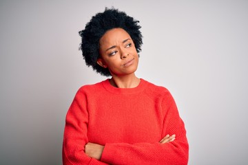 Young beautiful African American afro woman with curly hair wearing red casual sweater looking to the side with arms crossed convinced and confident