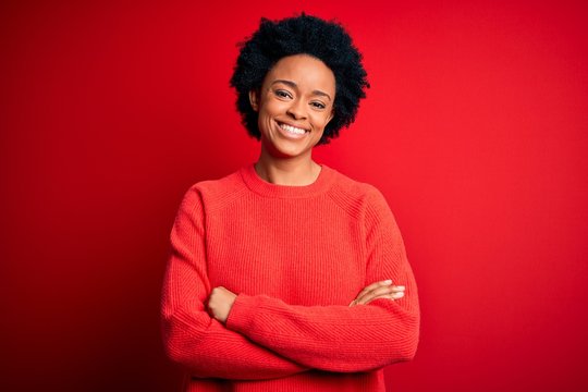 Young beautiful African American afro woman with curly hair wearing casual sweater happy face smiling with crossed arms looking at the camera. Positive person.