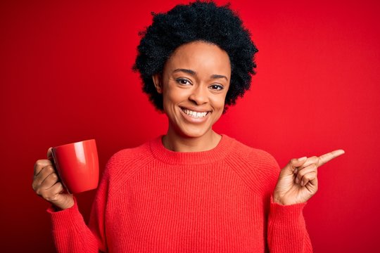 African American afro woman with curly hair drinking cup of coffee over red background very happy pointing with hand and finger to the side