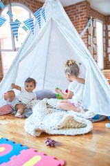 Beautiful toddlers playing inside tipi over blanket around lots of toys at kindergarten