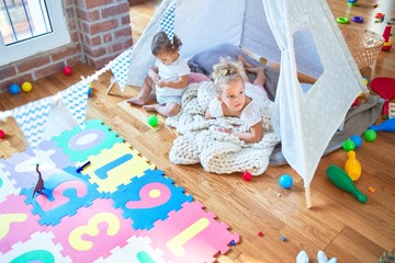Beautiful toddlers playing inside tipi over blanket around lots of toys at kindergarten
