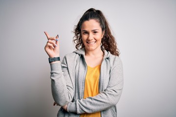 Young beautiful sportswoman with curly hair wearing sportswear over white background with a big smile on face, pointing with hand and finger to the side looking at the camera.