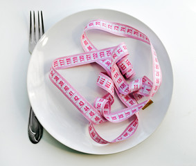 White plate, fork and pink measuring tape on a white background. Weight loss concept, baby on...
