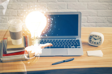 Computer on desktop in office with bulb icon hologram. Multi exposure. Concept of idea.