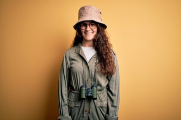 Young beautiful tourist woman on vacation wearing explorer hat and binoculars with a happy and cool smile on face. Lucky person.