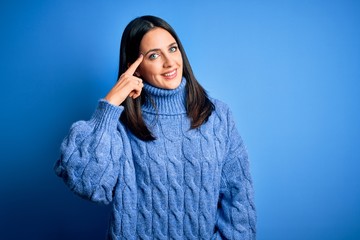 Young brunette woman with blue eyes wearing casual turtleneck sweater Smiling pointing to head with one finger, great idea or thought, good memory
