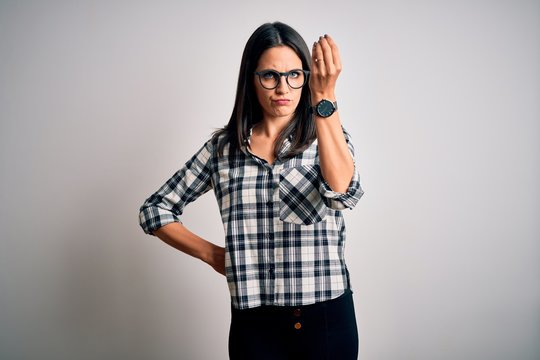 Young brunette woman with blue eyes wearing casual shirt and glasses over white background Doing Italian gesture with hand and fingers confident expression