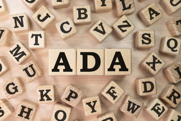 Word ADA on wooden blocks beige background top view, scattered cubes around random letters