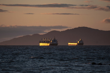 LARGE CARGO SHIPS AWAITING WAITING to get loaded on a coast during sunset golden hour in between mountains with scenic view at pacific ocean Pacific north west Vancouver Canada British Columbia 