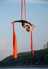 Beautiful and flexible female circus artist dancing with aerial silk on a sky background