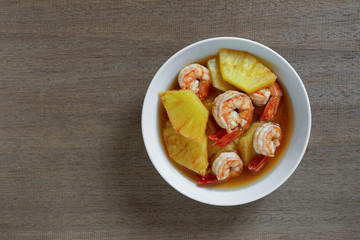 hot and sour pineapple soup with shrimp in a ceramic bowl on wooden table, top view. asian homemade style food concept.