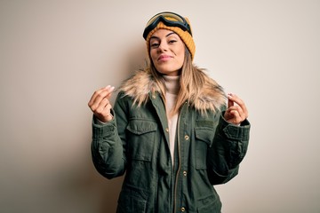 Young brunette skier woman wearing snow clothes and ski goggles over white background doing money gesture with hands, asking for salary payment, millionaire business
