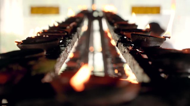 Closeup 4k video of long rows of burning candles and oil lamps on the altar of buddhist temple