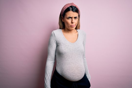 Young beautiful brunette woman pregnant expecting baby over isolated pink background skeptic and nervous, frowning upset because of problem. Negative person.