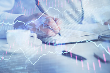 Double exposure of man's hands writing notes of stock market with forex chart.