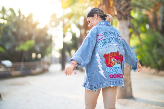 Young beautiful woman wearing denim jacket standing backwards at the town park