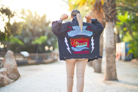 Young beautiful woman wearing denim jacket standing backwards at the town park